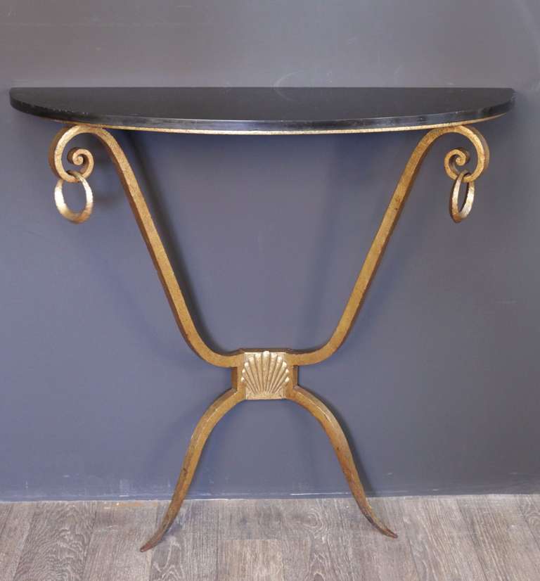Gilded wrought iron console with an original leaf black marble top adorned with two rings. The console is supported by two streamlined legs adorned with a shell.