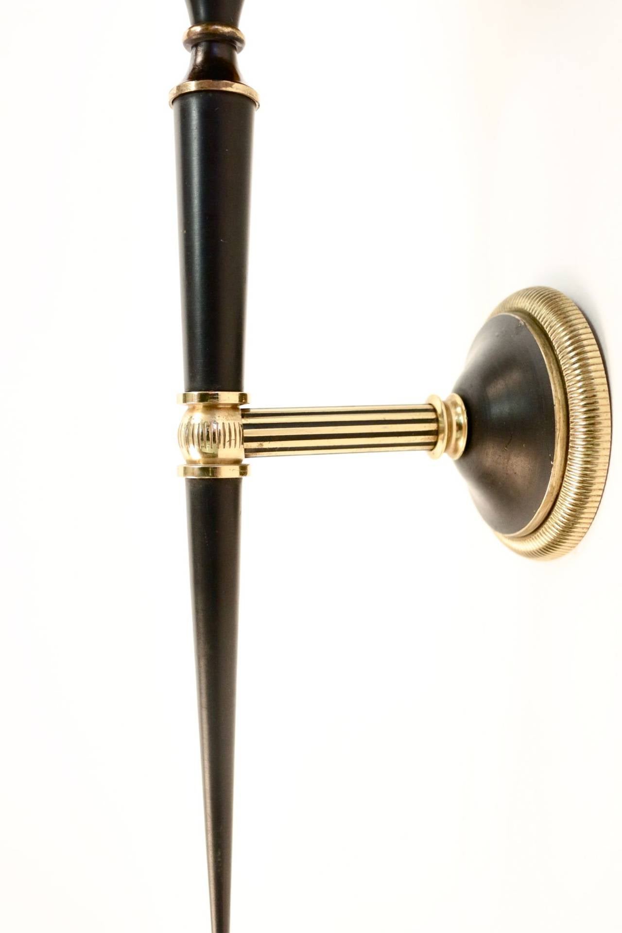 Elegant 1950s pair of sconces by Maison Lunel. Gilt and blackened brass. Alternate gilt and blackened brass on the trunk. The bottom enhanced by a small gilt brass whirligig. Tailored lampshade with gold color inside and black color outside. One