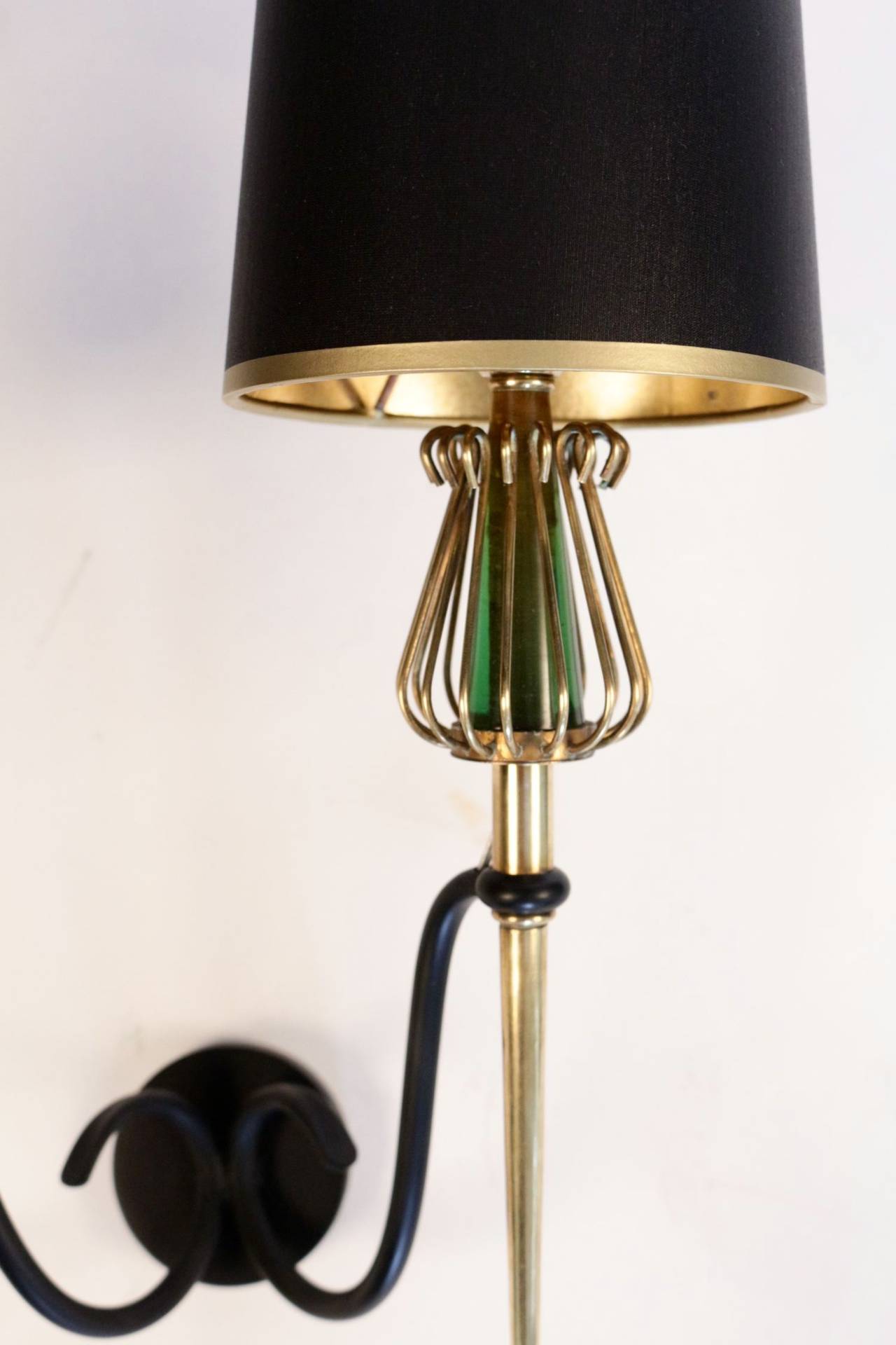 Large pair of 1950s sconces by Maison Lunel. Double lighted arm in gilt brass enhanced on the top by a brass wire cage framing a piece of green glass.

Tailored lampshade with gold color inside and black outside.