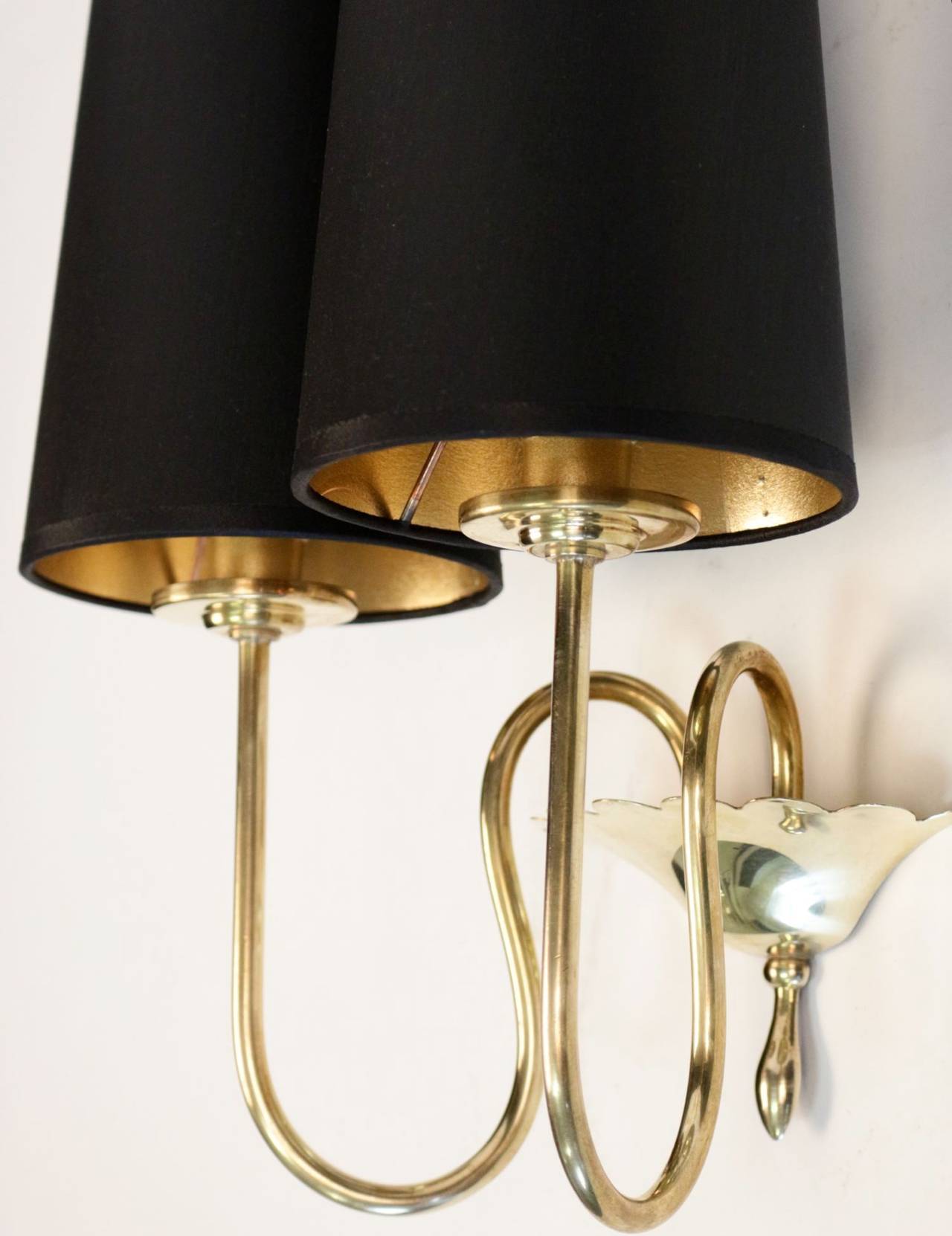 Pair of 1950s neoclassical sconces by Maison Arlus.
Serrated cup brass emphasized by two voluted rods serving as lighted arms. Lampshade made to measure, gold interior, black exterior. Two light arm per sconce.