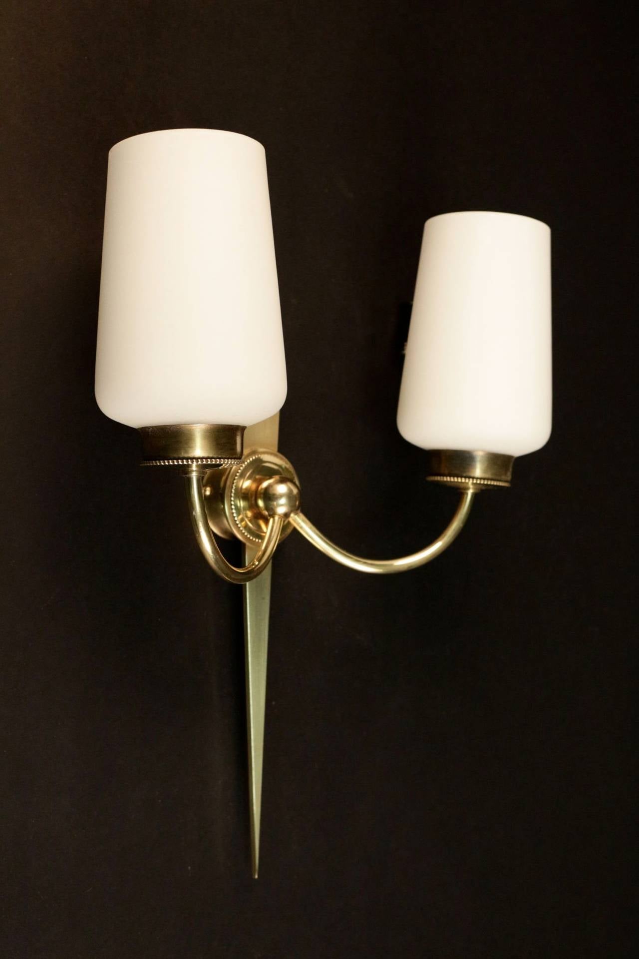 Pair of 1950s bronze sconces by Maison Arlus.
Elegant model composed of a bronze arrow shape asymmetrical plate.
Two lighted arms decorated with original opaline glass lampshades.
The oval lampshade holder is emphasized on its base by a circle