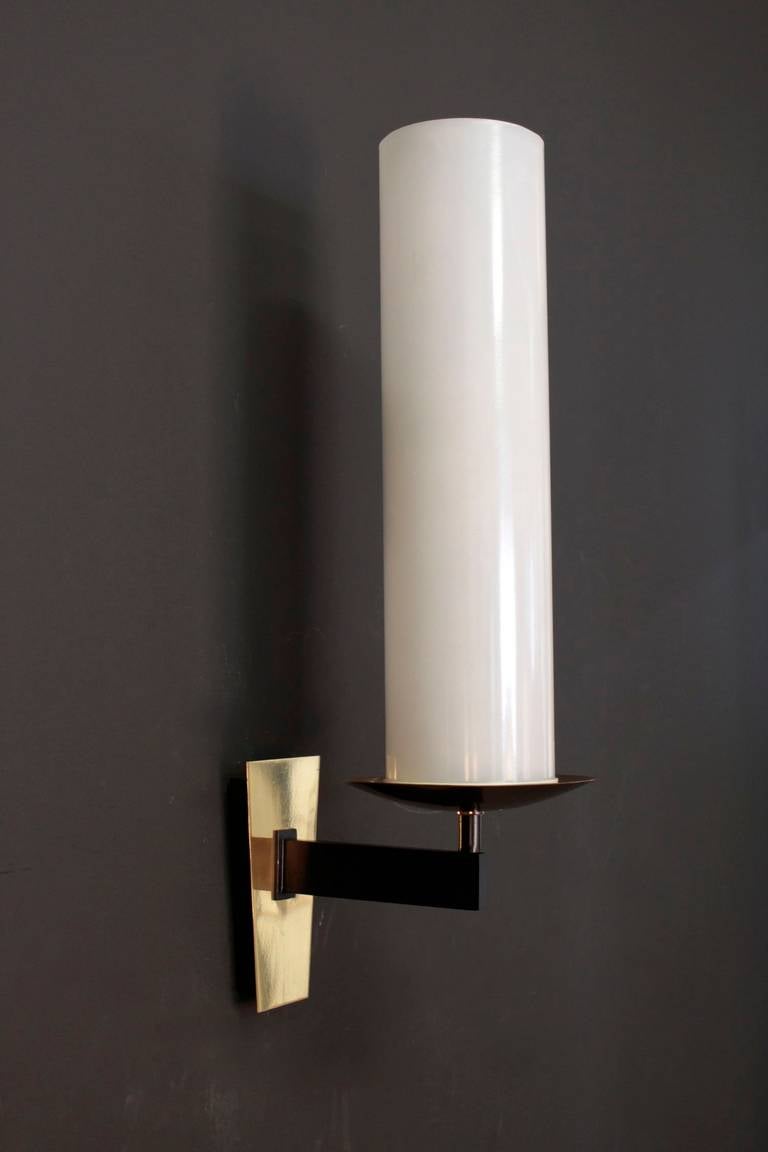 Large pair of 1950s sconces by Maison Lunel. The cylindrical opaline standing on a natural brass candleholder. Blackened brass arm highlighted by a natural brass trapeze mount. One lighted arm per sconce. Two bulbs in each opaline.
