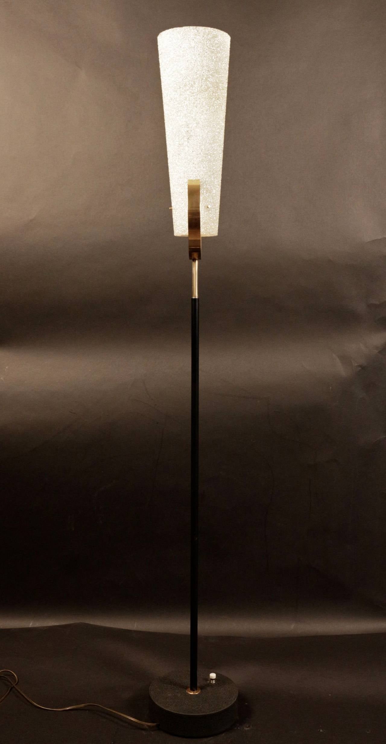 1950s Buckle Floor Lamp by Maison Lunel.

Composed of a blackened metal shaft enhanced by brass at the top and decorated with a large gilt brass buckle. The cylindrical base is enhanced by a circular brass plate. The cylindrical lampshade is in