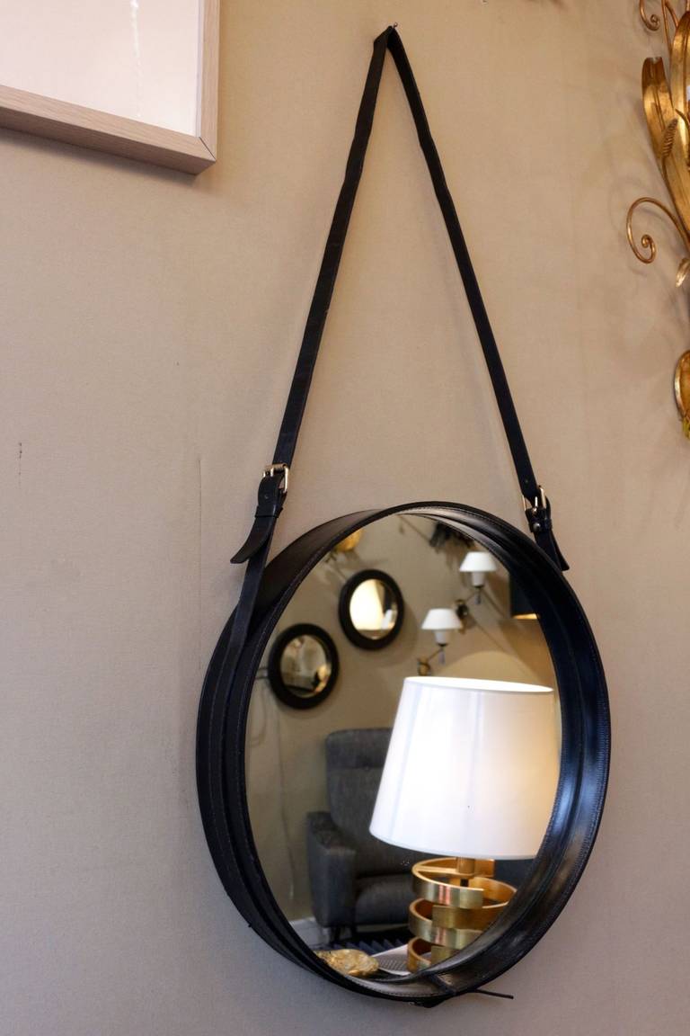 Large 1950s Jacques Adnet mirror in black leather emphasized by stitching and surrounded by a leather strap adorned with three brass buckles to adjust the height.