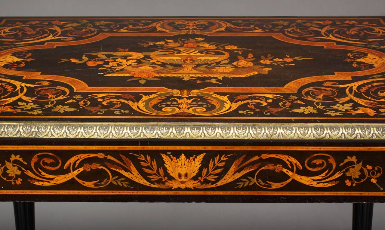 Origin: New York,
 
circa 1850.
 
Dimensions: Height 30″ (76cm),
width 50″ (127cm).
 
Technique: Marquetry.
 
Using exotic marquetry wood inlay the table portrays a central urn with roses and tulips and a bird with hatched eggs in a basket.