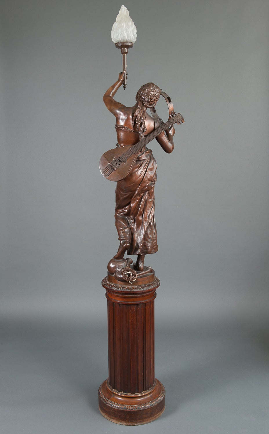 Cette très belle torchère figurative en bronze patiné grandeur nature représente une musicienne en tenue classique tenant une mandoline et une torche. Cette représentation symbolique de la Musique, s'inscrit dans l'œuvre allégorique de Coutan. La