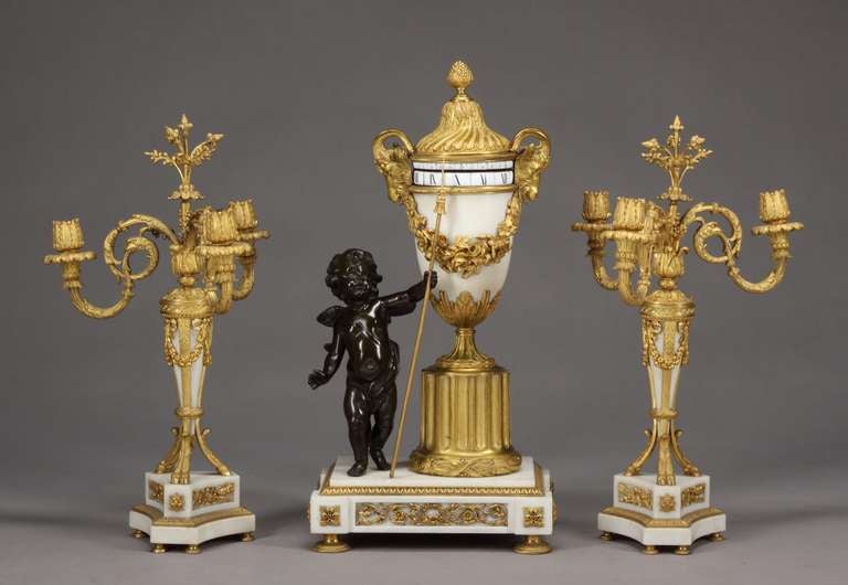 A rare and very fine 19th century French Louis XVI style ormolu mounted white marble 3-piece Rotary (Annular) clock set comprising a clock and a pair of 3 arms candelabra.
The urn shaped clock flanked by two Ram head handles, a patinated bronze