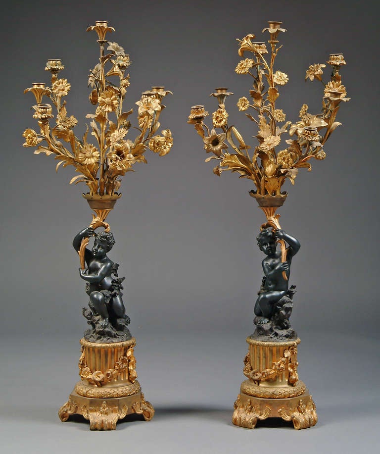 Pair of large French patinated and gilt-bronze figural Seven-light candelabras. each modeled as an exuberant putto supporting the leafy floral candle arms, raised on fluted pedestal bases.