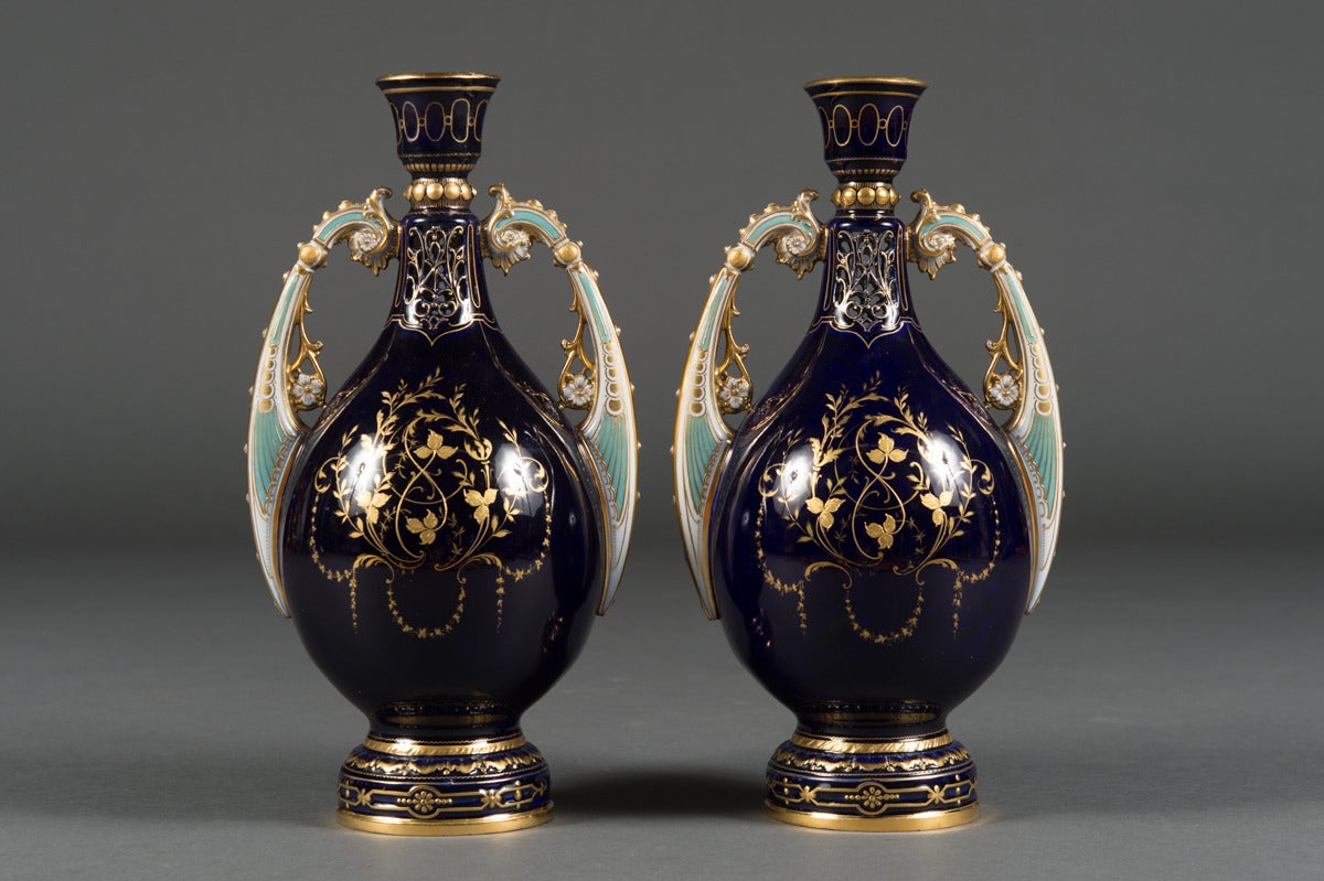 A Pair of Antique Austrian Royal Vienna Style Jeweled Cabinet Vases

Each vase with a central painting of two maidens surrounded by enamel and gold leaf designs under a pierced neck. The unique handles with a light green color attached to the