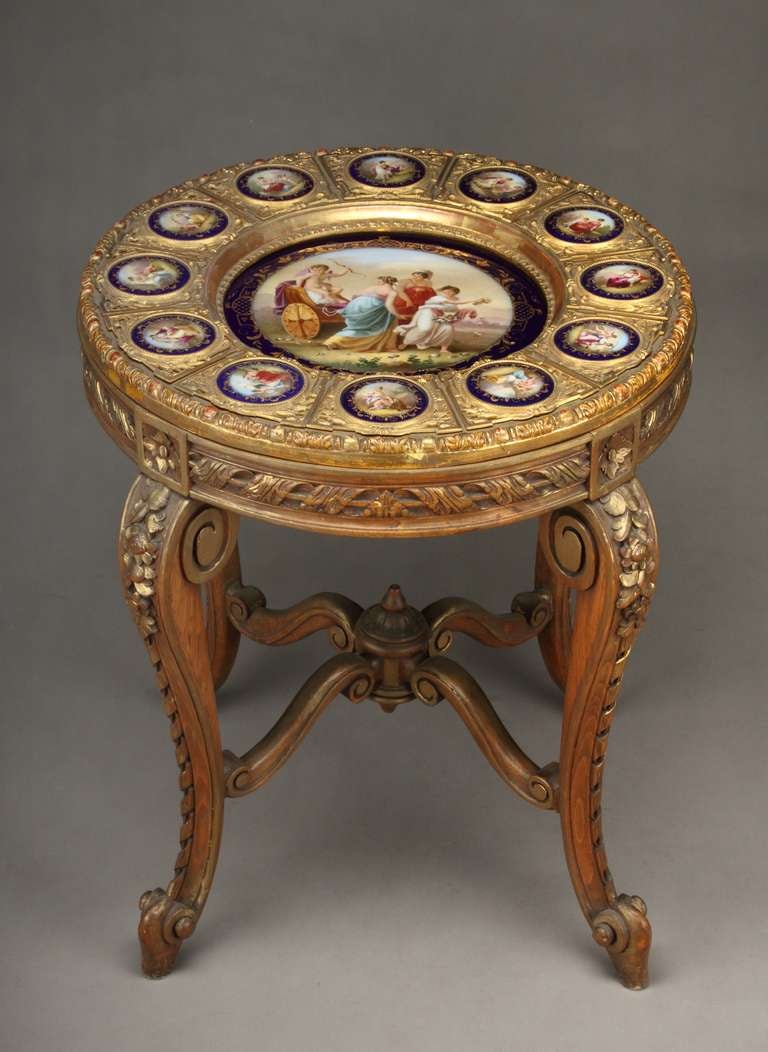 A 19th century Austrian Royal Vienna Porcelain table. 

The center hand-painted plaque depicting cupid getting pulled on a carriage by three nymphs. It surrounded by 12 smaller hand-painted circular plaques sitting on its original hand-carved wooden