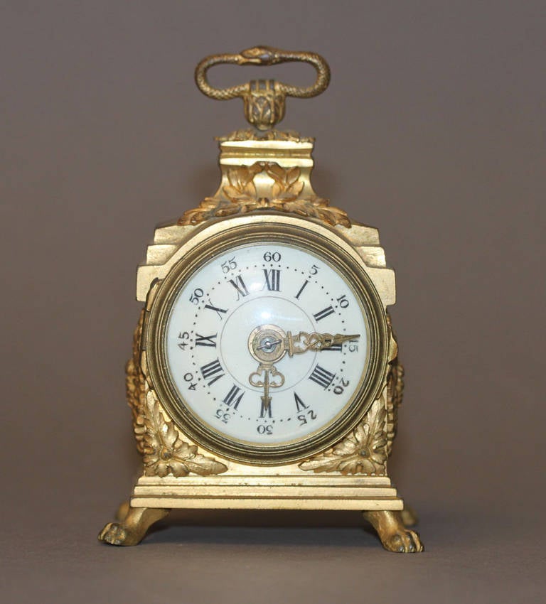 A Late 19th Century Gilt-Bronze Miniature Carriage Clock

The snake handle over a porcelain dial with Roman & Arabic numbers and paw feet with well decorated case smothered in acanthus and ribbons, the white enamel dial with black painted
