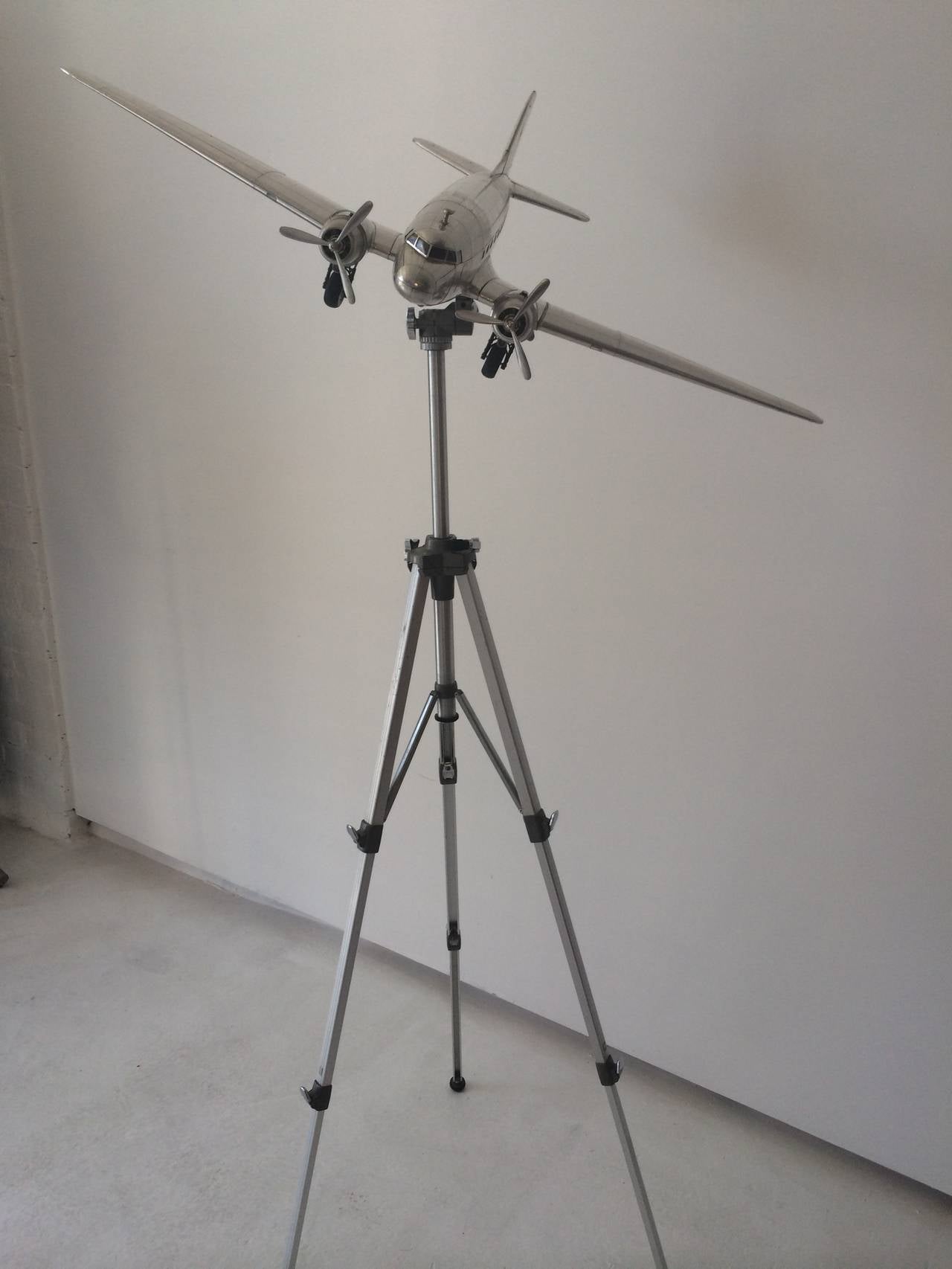 Beautiful 1980s DC-3 airplane scale model, aluminum, with 1940s tripod.
The tripod can be adjusted at the swivel and in height up to approximately 70 inches.