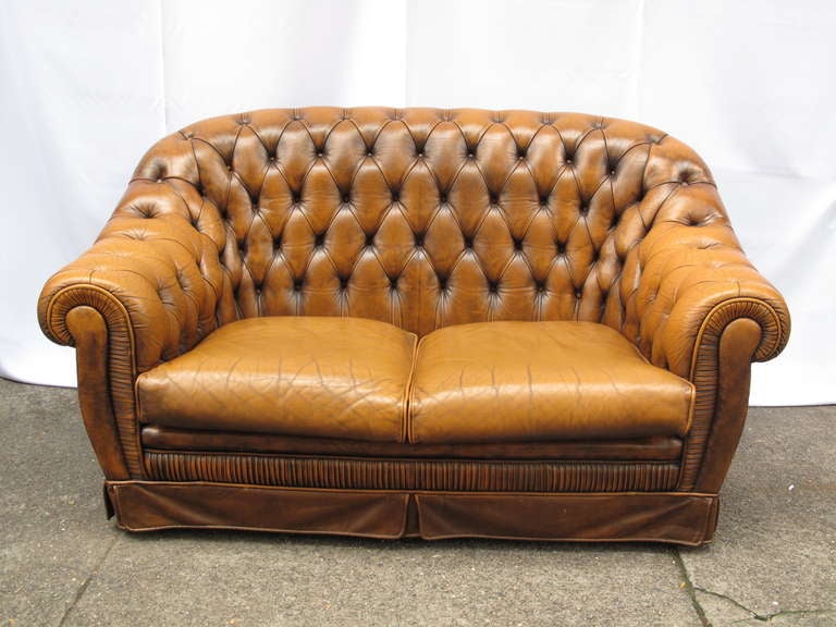 Caramel leather high back button tufted loveseat.  Chesterfield style with two loose cushions. Skirted base.