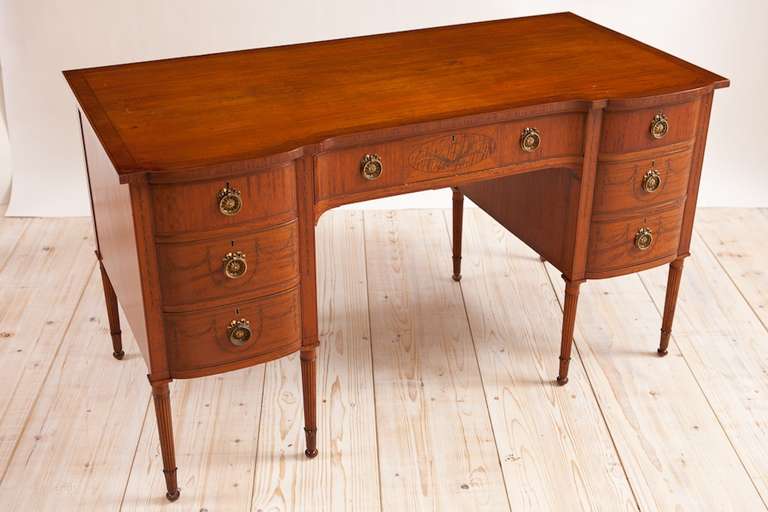 English Edwardian satinwood knee hole desk with bell flower swag decoration, circa 1900. What a beautifully proportioned and esthetically pleasing desk. It provides ample work area but appears diminutive in scale because of its fine legs and the