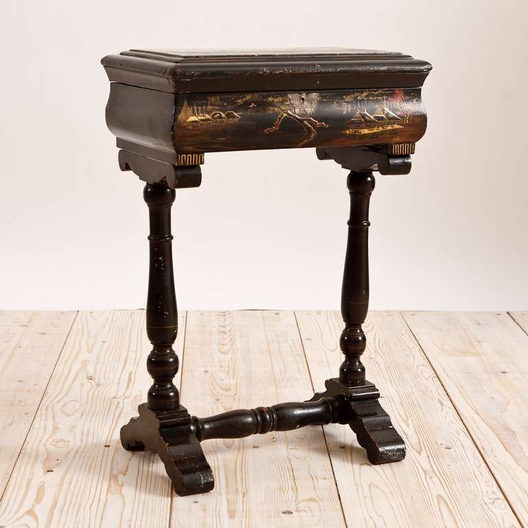 Black-lacquered chinoiserie work table with polychrome painted scenes on trestle base with hinged lift-top exposing lidded compartments and open cubbies, with original key plate in the form of a butterfly, China, circa 1840.

Measures: 18 1/4