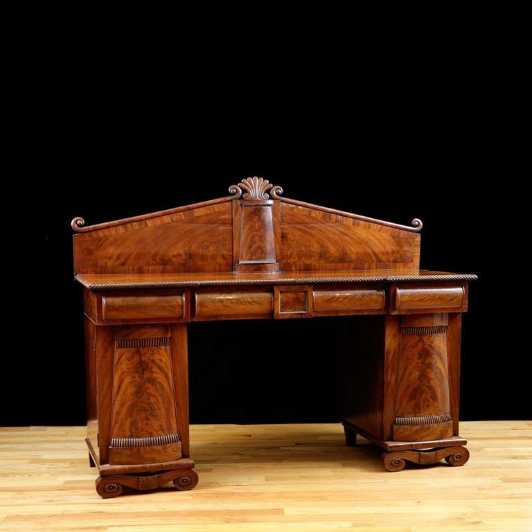 English Regency pedestal base sideboard with scroll foot supporting tapered pylon form pedestals and beautiful back splash with palmette carving terminating above a small pylon that matches pedestal fronts. Three drawers across the front and