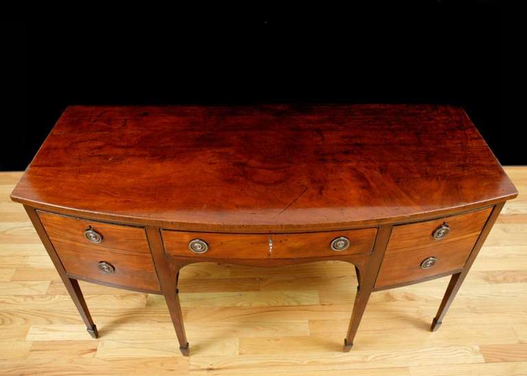 Bella credenza di Giorgio III in mogano con fronte arcuato e gambe quadrate affusolate che terminano con piedi a vanga, con cassetto centrale a fregio affiancato da due cassetti a celletta. Il piano è composto da un'unica tavola massiccia di mogano,