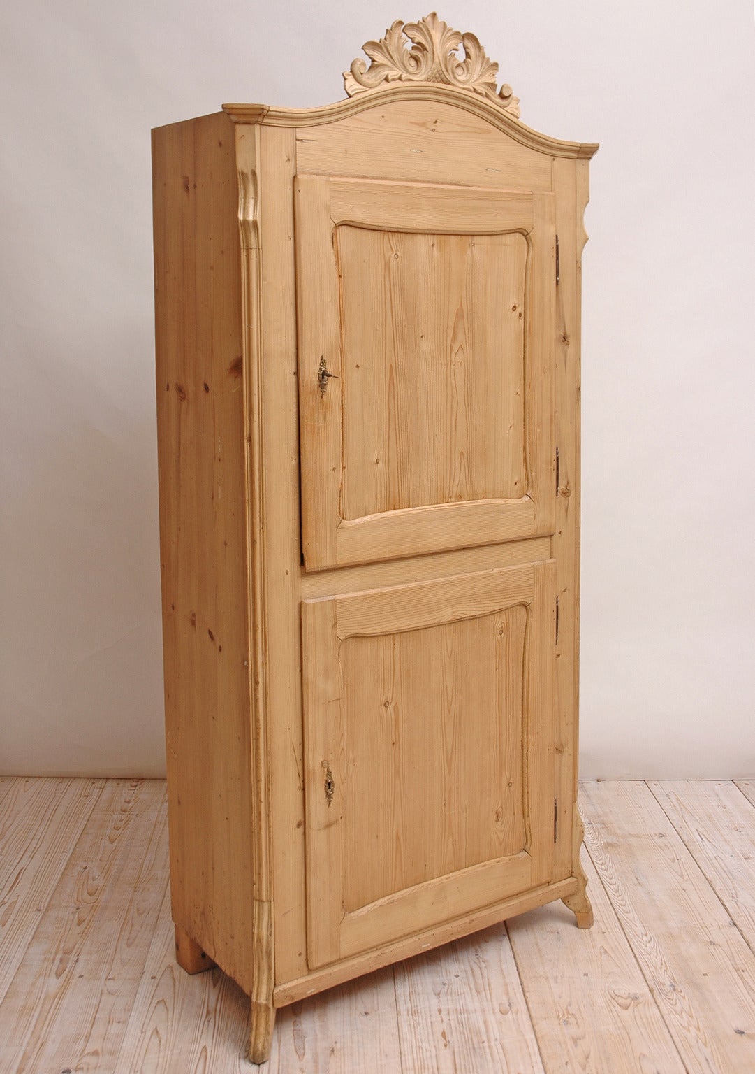 A narrow and tall pine cupboard with two doors, one above the other on slipper feet with pierced and carved foliate bonnet. Interior has blue/green casein paint. A lovely storage piece in a child's room or playroom. Also makes a charming kitchen