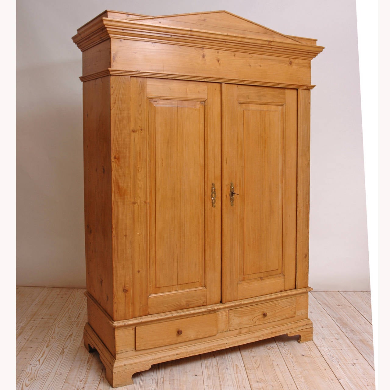 A fine German pine armoire with pegged construction from the Empire/ Biedermeier period with pediment top, two raised paneled doors, two exterior drawers and resting on bracket feet. Interior was modified by our workshop to include retractable doors