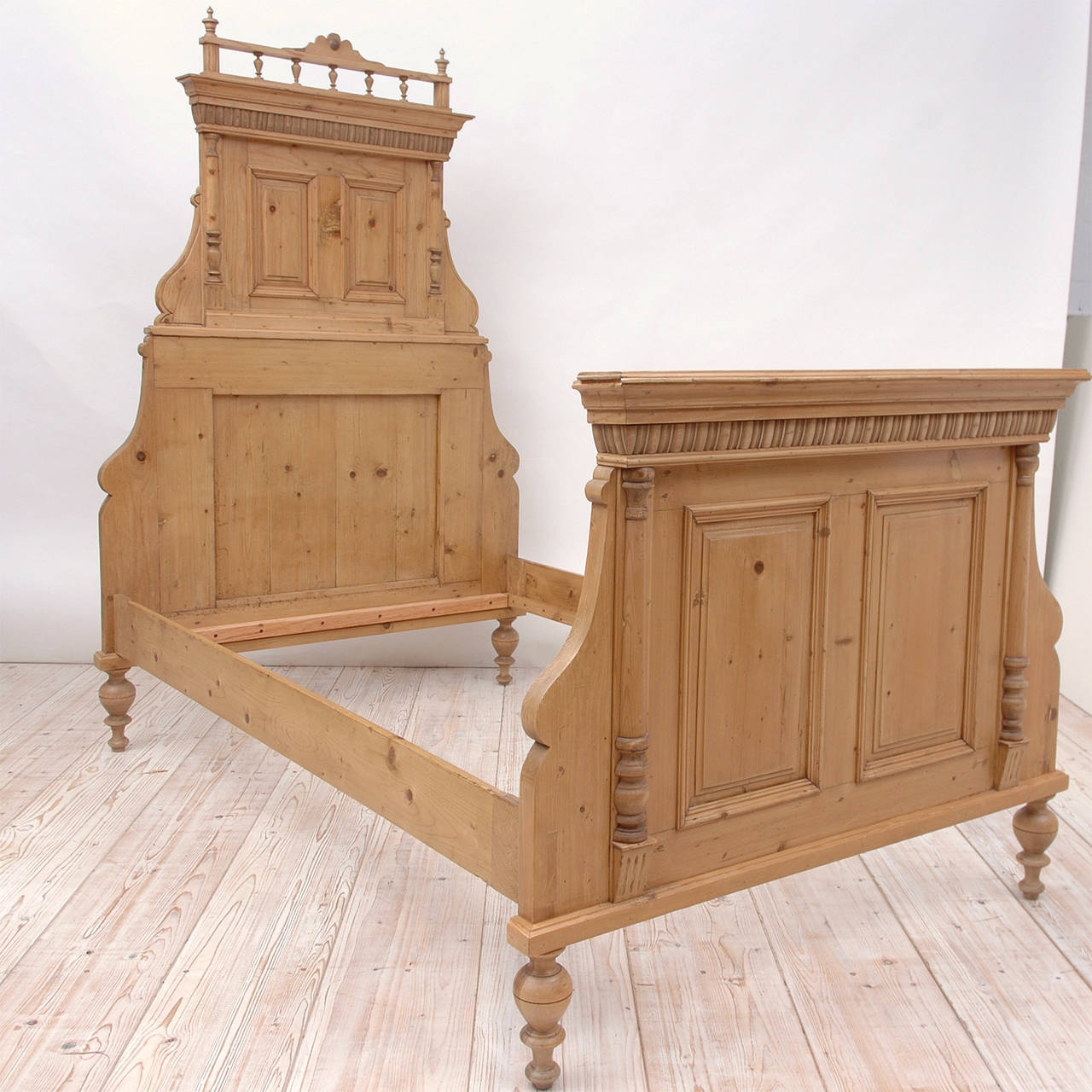 From the Austria-Hungarian Empire, an exceptional pair of beds in pine with elaborate embellishments, featuring recessed panels with moldings that are flanked by pilasters on the foot boards and carved bonnets with galleries above the paneled