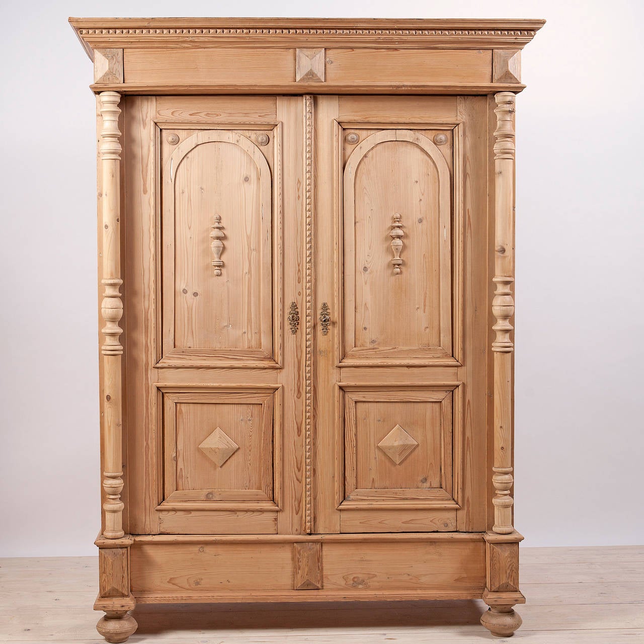 A European 2 door pine armoire with full columns and turned bun feet. Paneled doors feature appliques and interior has adjustable shelving. From the German Grunderzeit period c. 1895

Measures: 60