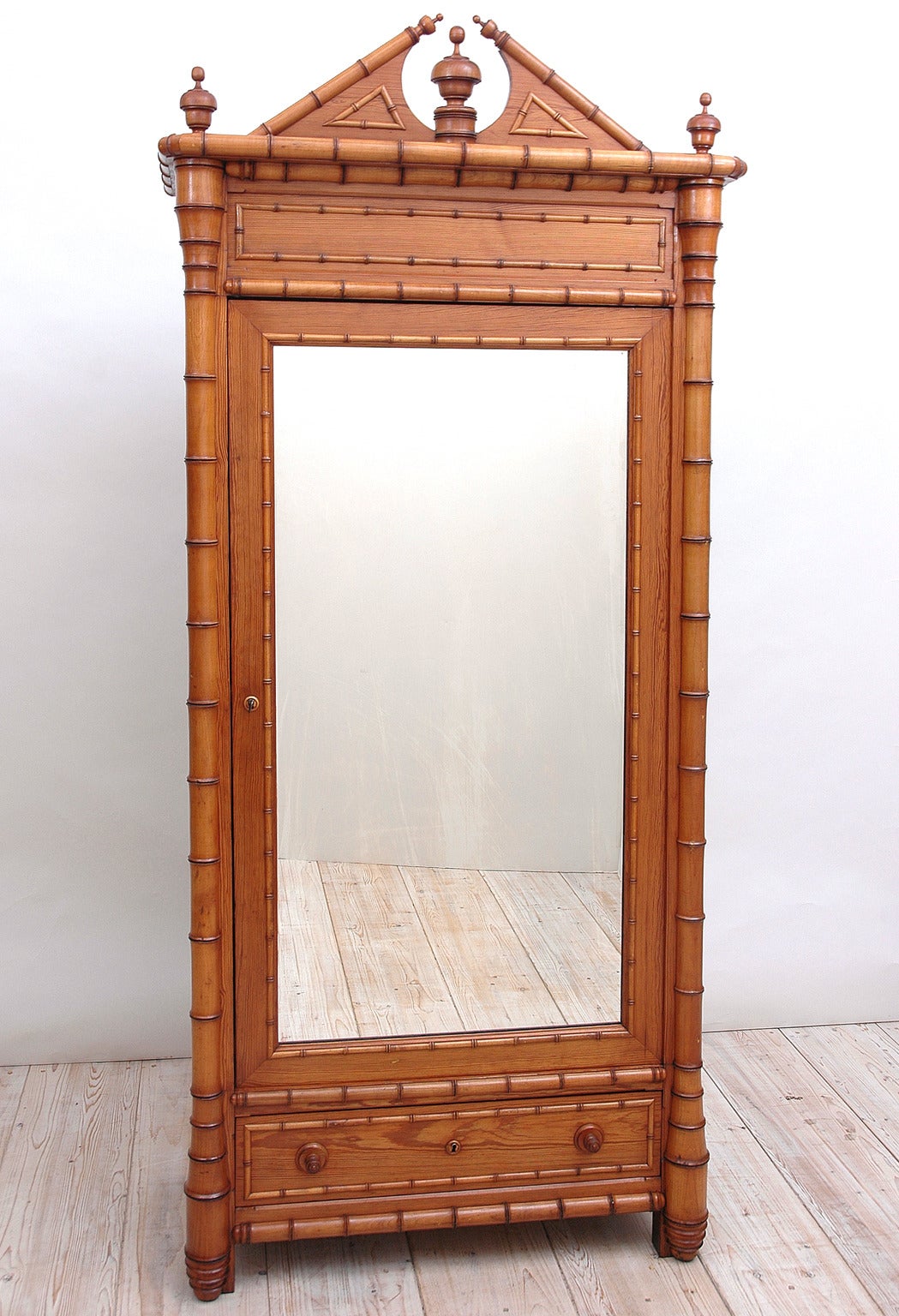 A rather exceptional faux bamboo armoire in maple and pine with split pediment top and steeple-turned finials on cornice and a single mirrored-door with one exterior drawer and four interior shelves. Offers working lock and key and original turned