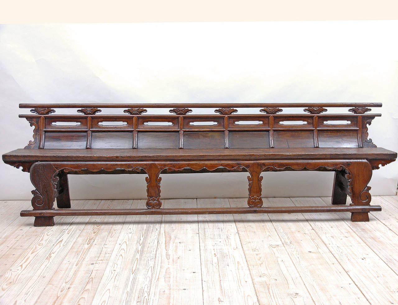 From the Shanxi province in China, an exceptionally beautiful and long bench in elm wood with paneled concave back and pierced carvings between rails and upper panels, carved apron and legs. Seat is composed of one long wood plank. Has a rich and