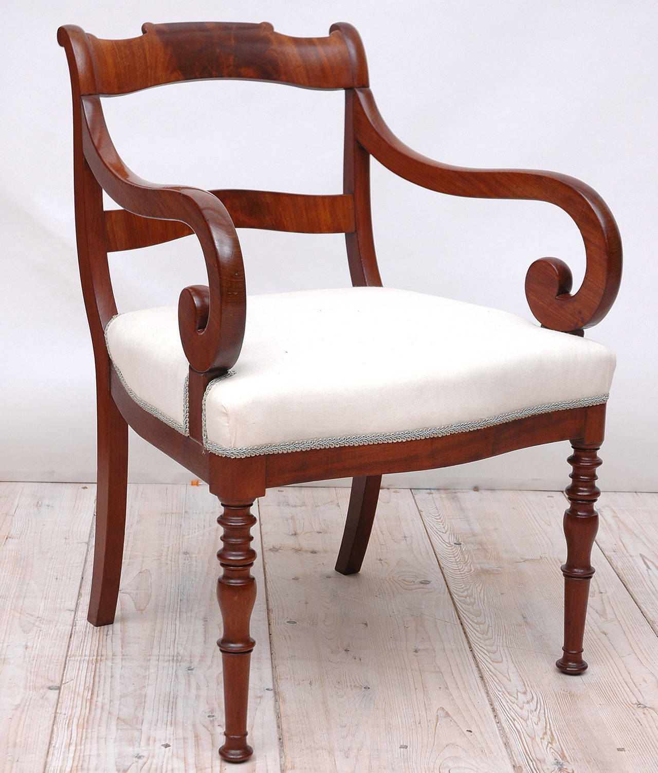 A fine armchair or fauteuil in premium figured mahogany with slat-back, scroll arms, upholstered seat, turned front legs and saber back legs. A beautifully proportioned and well-crafted, solid chair that would make an excellent desk or accent chair.