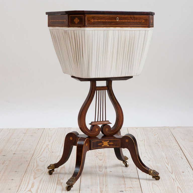 English Regency sewing table with marquetry, circa 1820. A fine example in Cuban mahogany with satinwood inlays whose hinged-top opens to access pleated silk basket with lyre pedestal resting on curved saber feet and bronze lion's paw