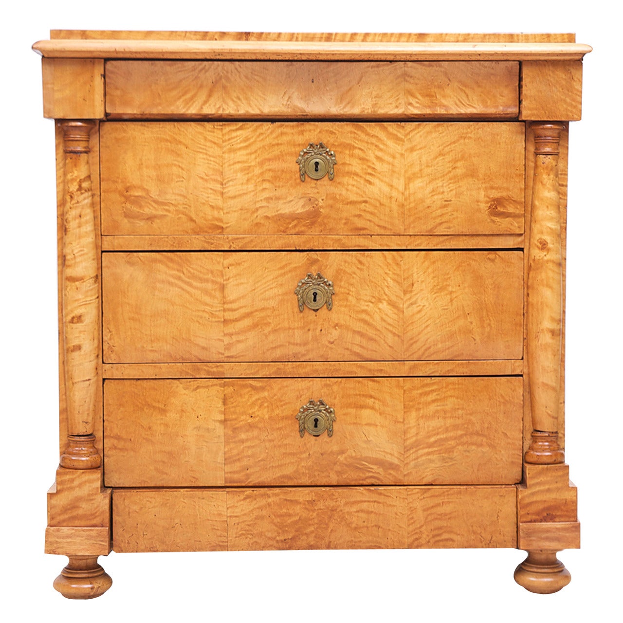 A very handsome and small Swedish Biedermeier chest of drawers in book-matched quilted birch that is of a golden honey-color. Offers a total of five drawers, with three flanked by turned pilasters and two that are somewhat secret as they form part
