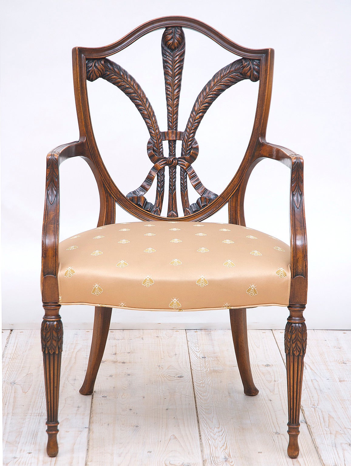 A pair of lovely shield-back armchairs in mahogany with open carving of three ostrich plumes tied by a bow, a reference to the Prince of Wales who was the Prince Regent before becoming King (George III). Offers a wide upholstered seat and turned,