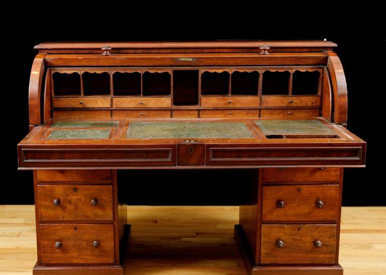 A fine English pedestal desk in mahogany with cylinder-top opening to an ample desk surface offering a row of open cubbies above a row of four small desk drawers. Pull-out desk surface has four original, tooled green-leather inset panels, the center