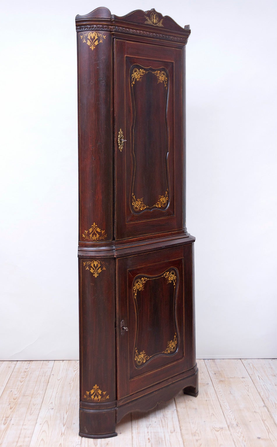 A rare and stately corner cupboard with the original faux-boix finish and hand-painted gold foliate and flower design around the recessed door panels and rounded sides, with a painted butterfly on the center of the tiara-top. Bremen, Germany, circa