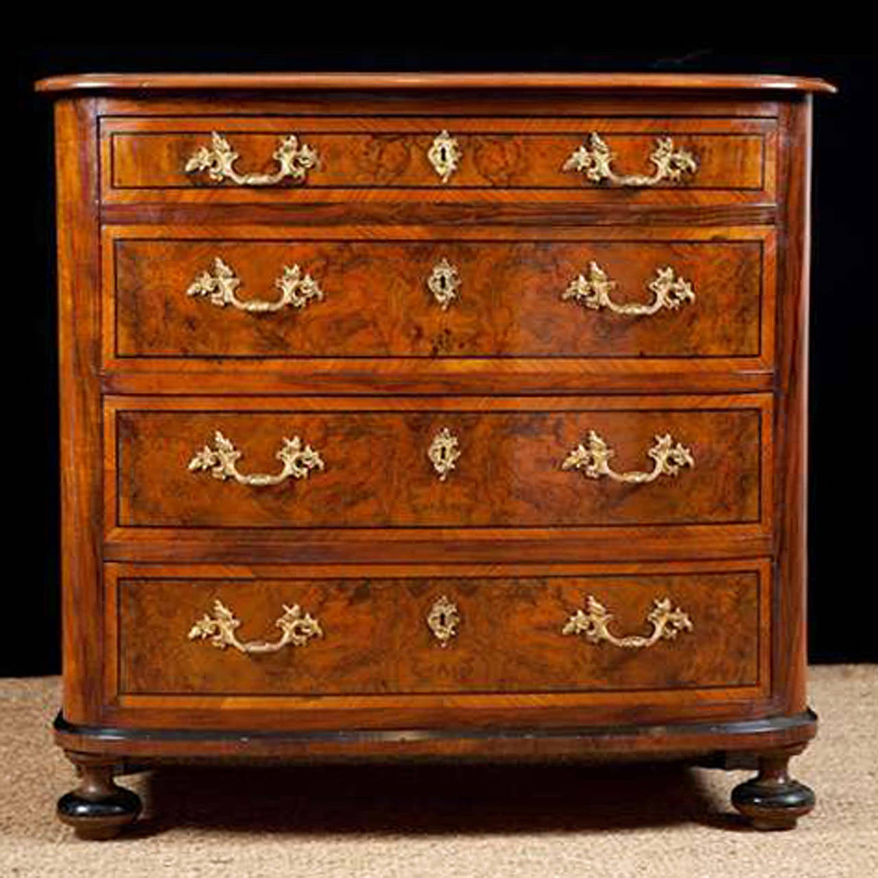 A handsome chest of drawers in walnut with panels in burled walnut and ebonized details throughout. Chest rests on original turned front feet and square back feet and features a bowed front with four storage drawers, offering a shallower one at the