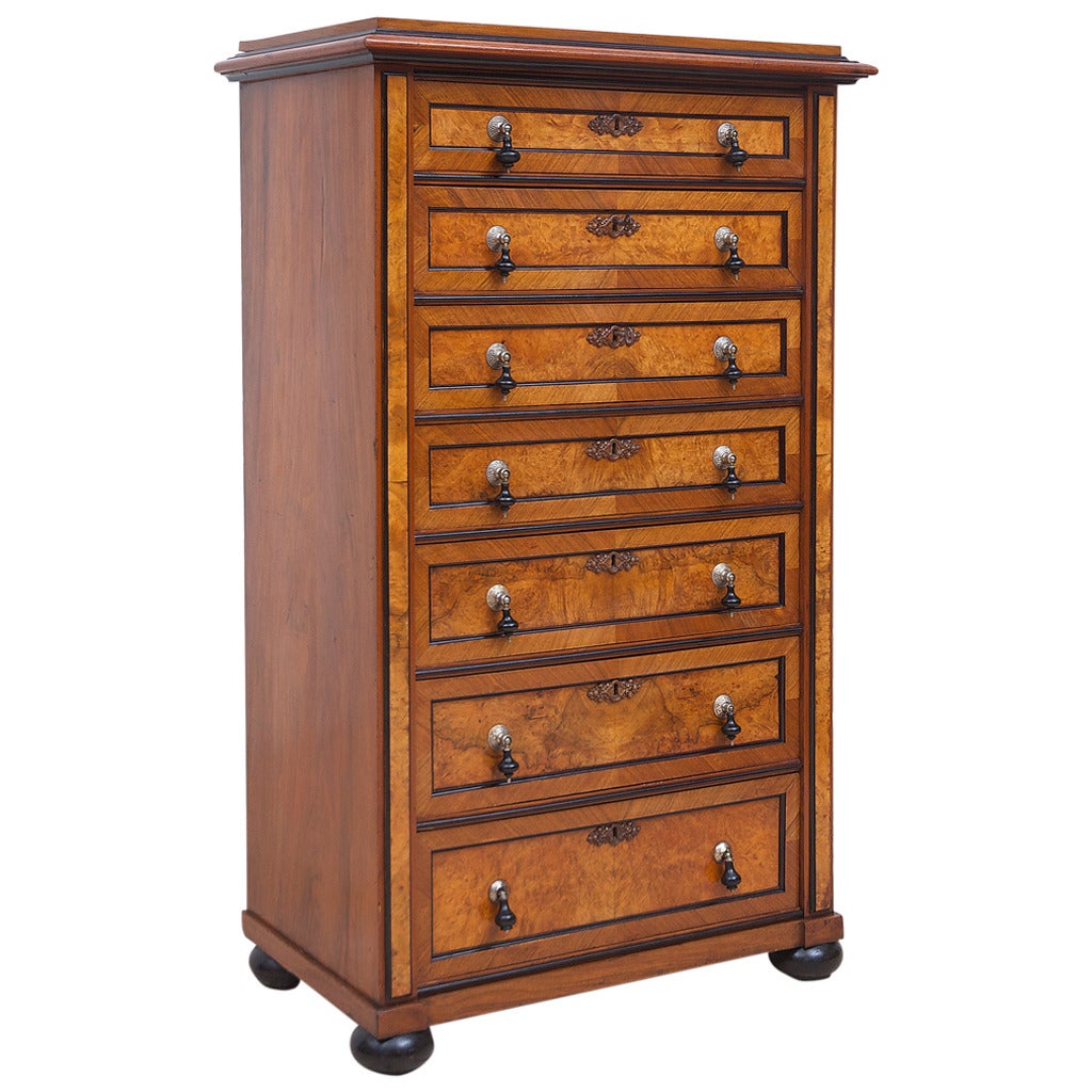 A beautifully crafted Scandinavian tall chest with seven graduated drawers in figured walnut with recessed panels and ebonized moldings on ebonized bun feet. Offers original tear-drop pulls with nickel backplates and original carved wood key plates.