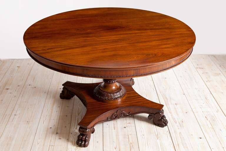 A beautifully executed tilt-top table. Features a round top with apron trimmed with a beaded border resting on urn-turned pedestal embellished with carved palmettes on quatre-form base ending in carved lions & paw feet. Of Cuban mahogany, considered