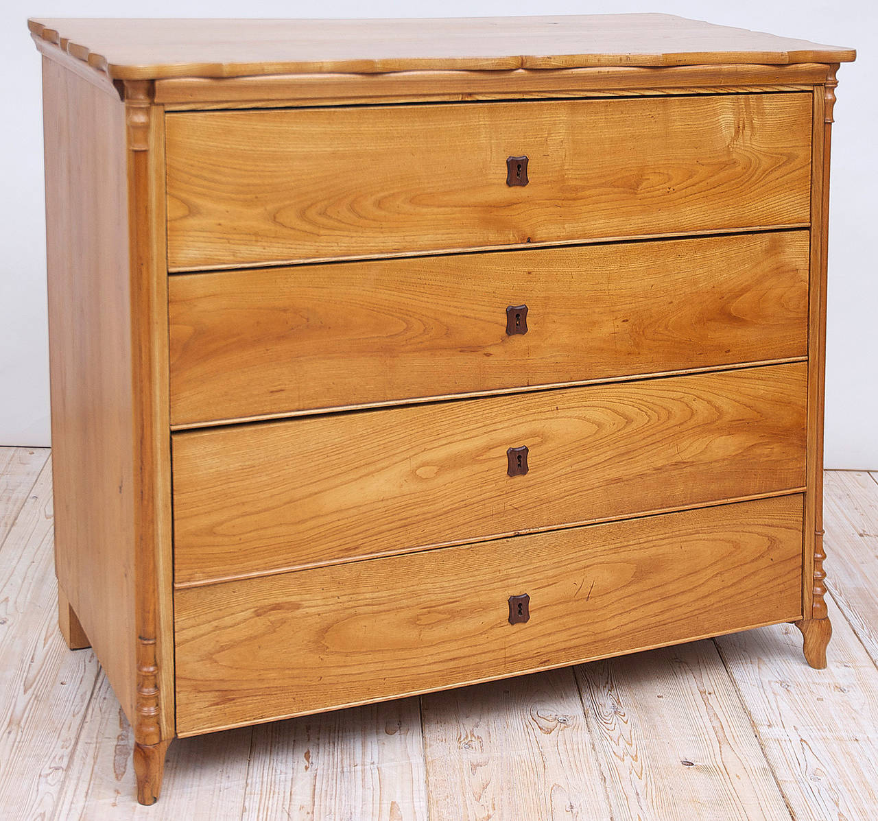 A very handsome early Biedermeier chest in ash with scalloped top, thinly-turned half-columns on chamfered corners, terminating in short Grecian style feet. Offers four drawers of staggered depths with original ebonized wooden key plates, original