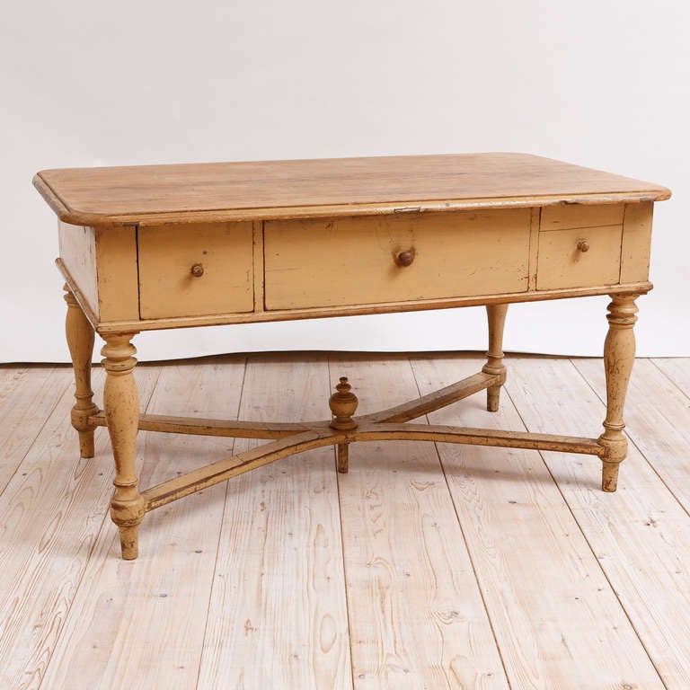 A very charming farmhouse table in the original yellow ochre paint with three drawers with the original wooden pulls, turned legs with 