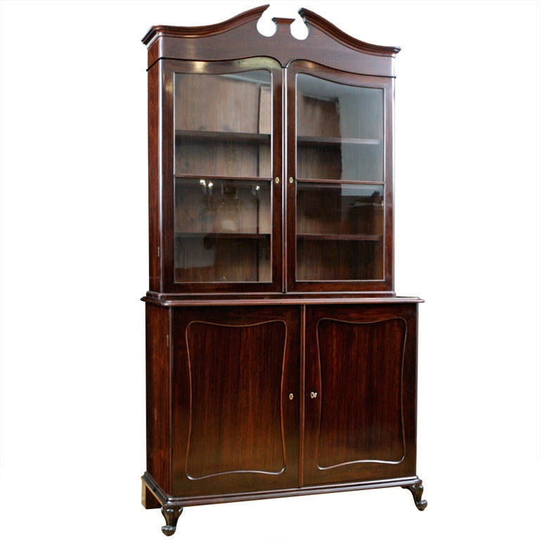 This cabinet displays an exceptional level of craftsmanship. Made of exotic & rare rosewood, this fine & tall Louis Philippe bookcase or china cupboard has a carved pediment top with glazed door panels on the top cabinet for displaying china or
