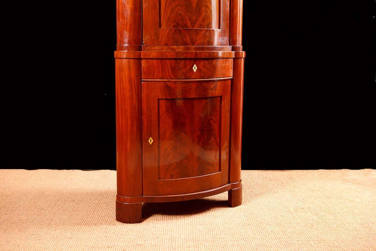 An exceptional Biedermeier corner cabinet with bowed front in book-matched West-Indies flame mahogany. Features arched bonnet top, with two cabinets separated by a center drawer. Denmark, circa 1830. Comes with working locks & key, and offers