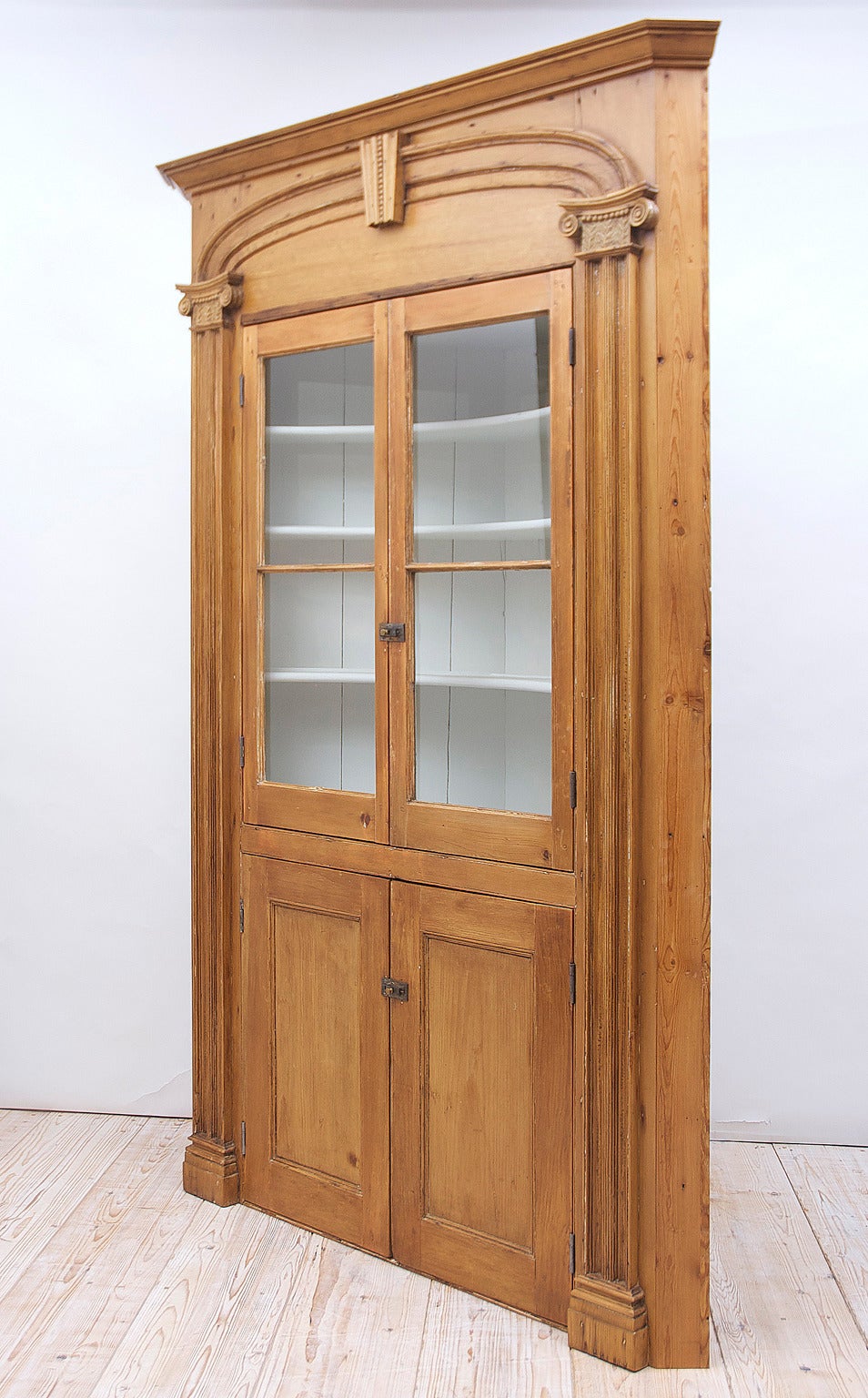 An American Federal Corner Cupboard in pine with painted pale grey interior. Features carved and fluted pilasters with Doric capitals decorated with the tree of life motif, flanking cabinet with glass-mullioned upper doors above wooden-paneled lower