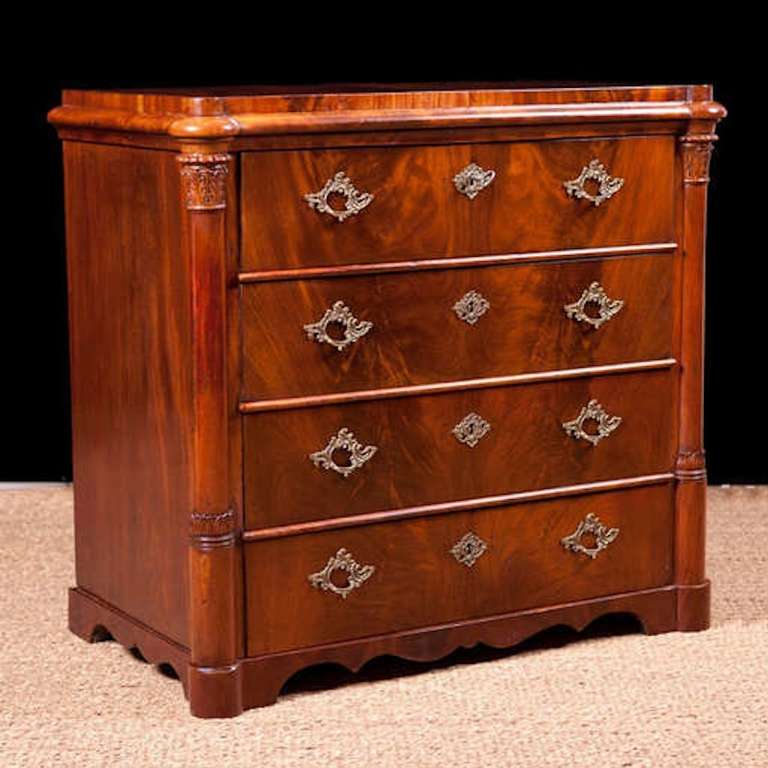 Neoclassical commode in mahogany with three drawers flanked by pillars with carved acanthus leaves on capitals. Brasses may not be original to the chest but work well with the form. The scale of this chest makes it suitable as an end table or