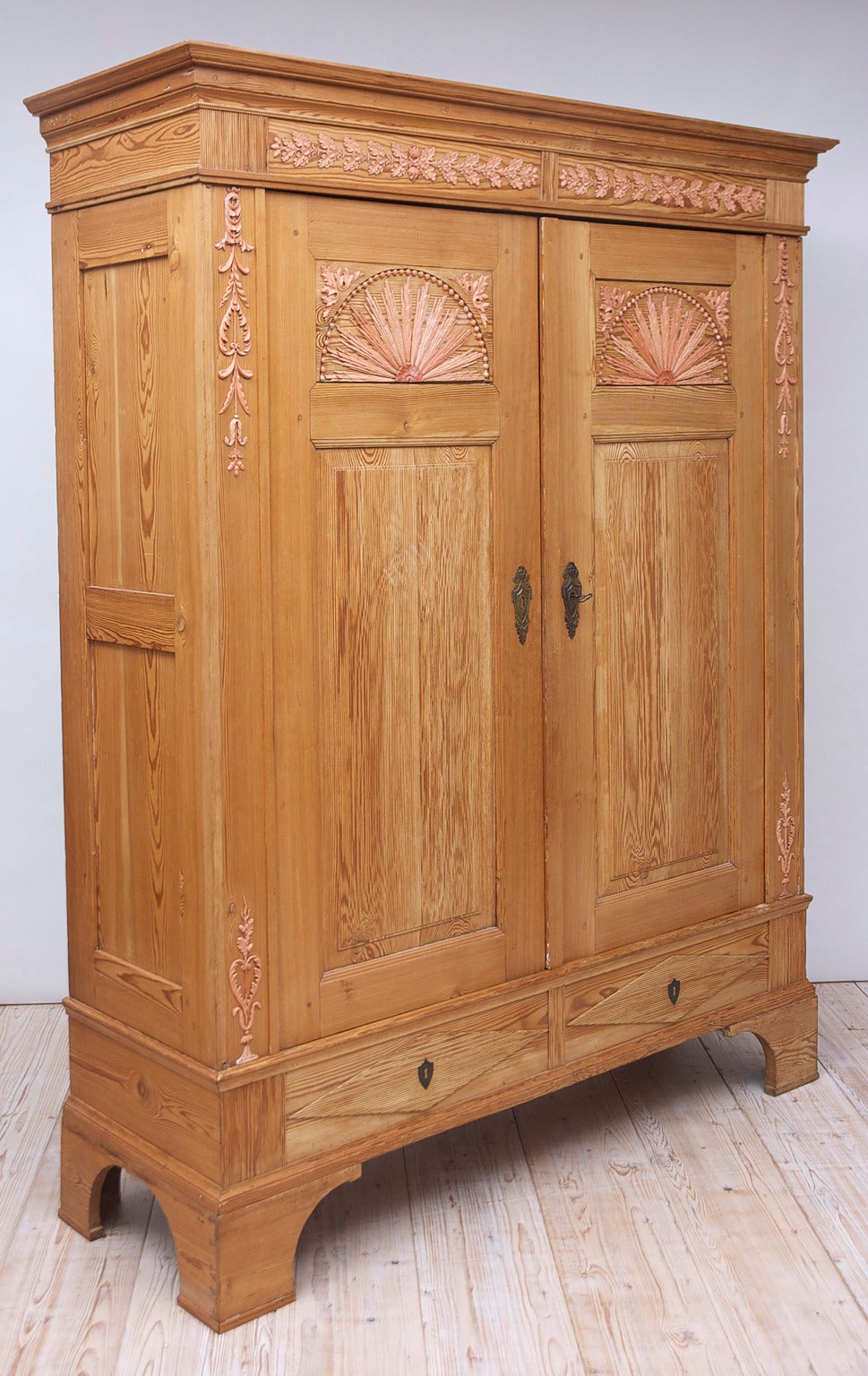 This exceptional one-of-a-kind armoire from the area of Bremen has the original pink gesso appliqués, circa 1790.  Fabricated from a beautiful knot-less dense pine, the carved ribbed panels on the doors and drawers and the strong bracket feet are