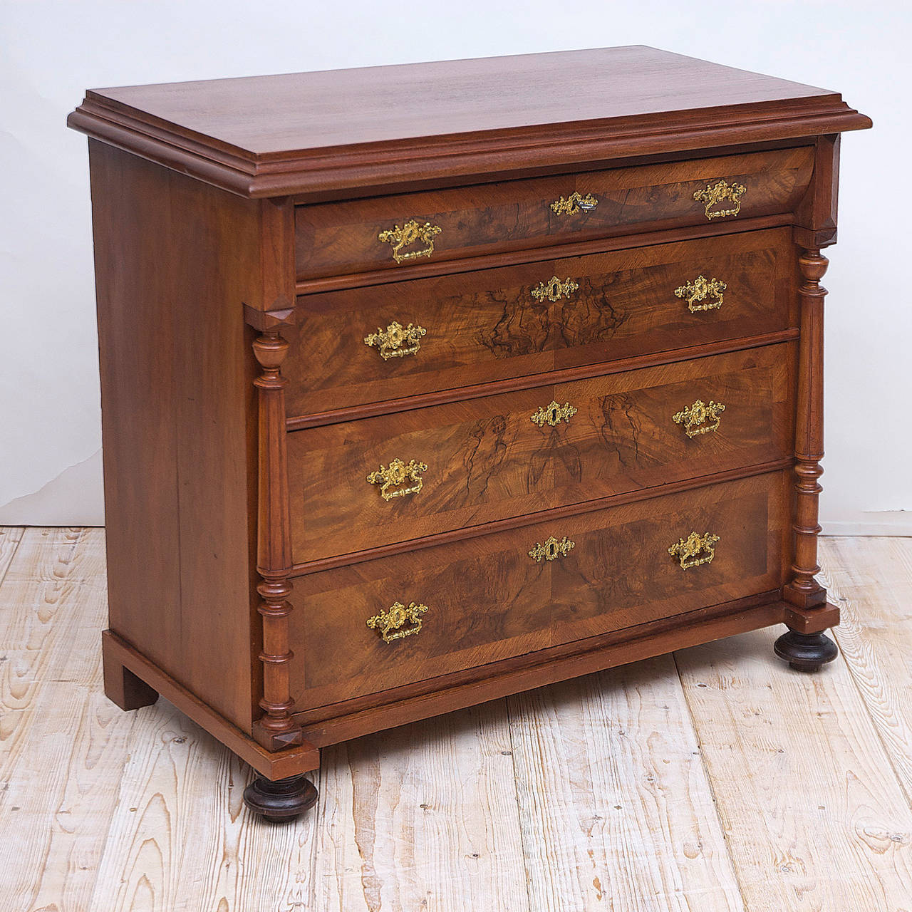A chest with four drawers in figured walnut, with turned fluted columns and original bun feet. Top drawer has convex front with interior, sliding pine drawer covers. Features original brass pulls and key plates, working locks, and one key. From the