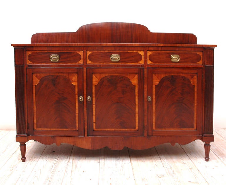 A beautiful American Sheraton sideboard in mahogany and satin wood featuring original pulls and reeded legs. Original finish lightly restored and waxed with a hard carnuba and bees wax finish. Original back splash is available which is slightly