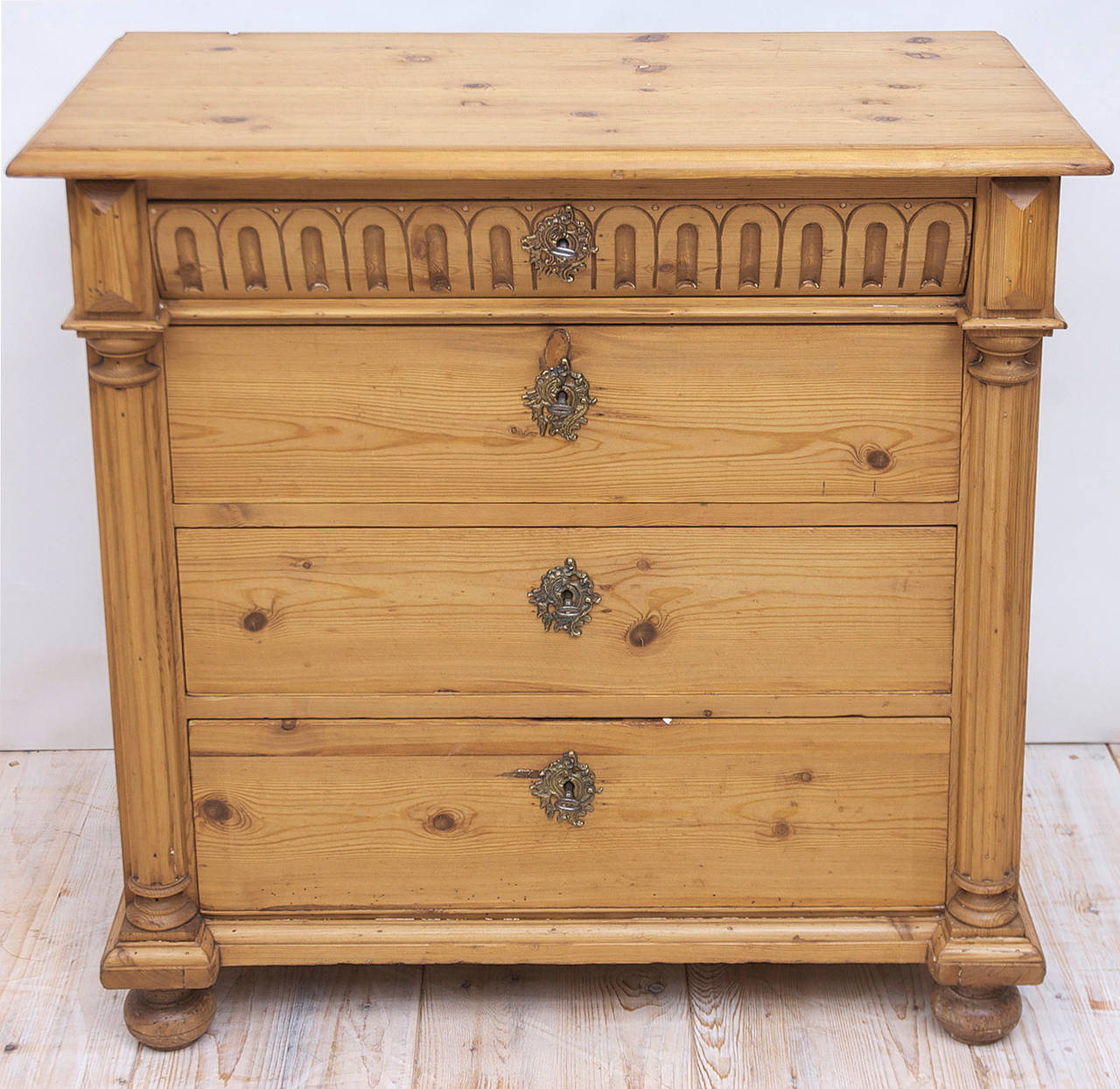 A charming chest in pine with four drawers, the top drawer with carved convex front, followed by three deeper drawers flanked by fluted half columns, and resting on original turned birch feet. Offers four working locks with four keys. Sweden, circa