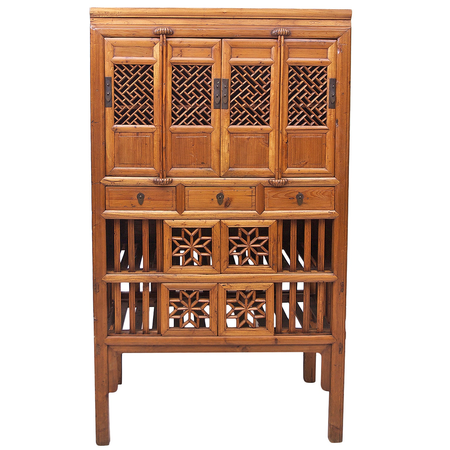 A charming cupboard in elm wood with four cabinet doors with open lattice carving above three drawers, which are followed by two separate compartments whose shelves have wide open slats as do the front walls flanking each set of sliding doors that