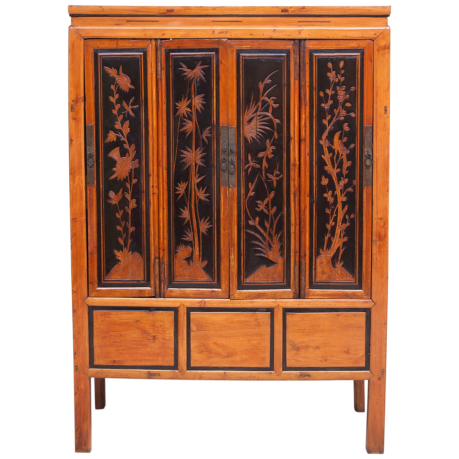A lovely Chinese cabinet in elm with four doors whose panels show a carved scene of vegetation representing each of the four seasons in relief. The amber color of the wood, as well as the cabinet's architecture & scenes are enhanced by the ebonized