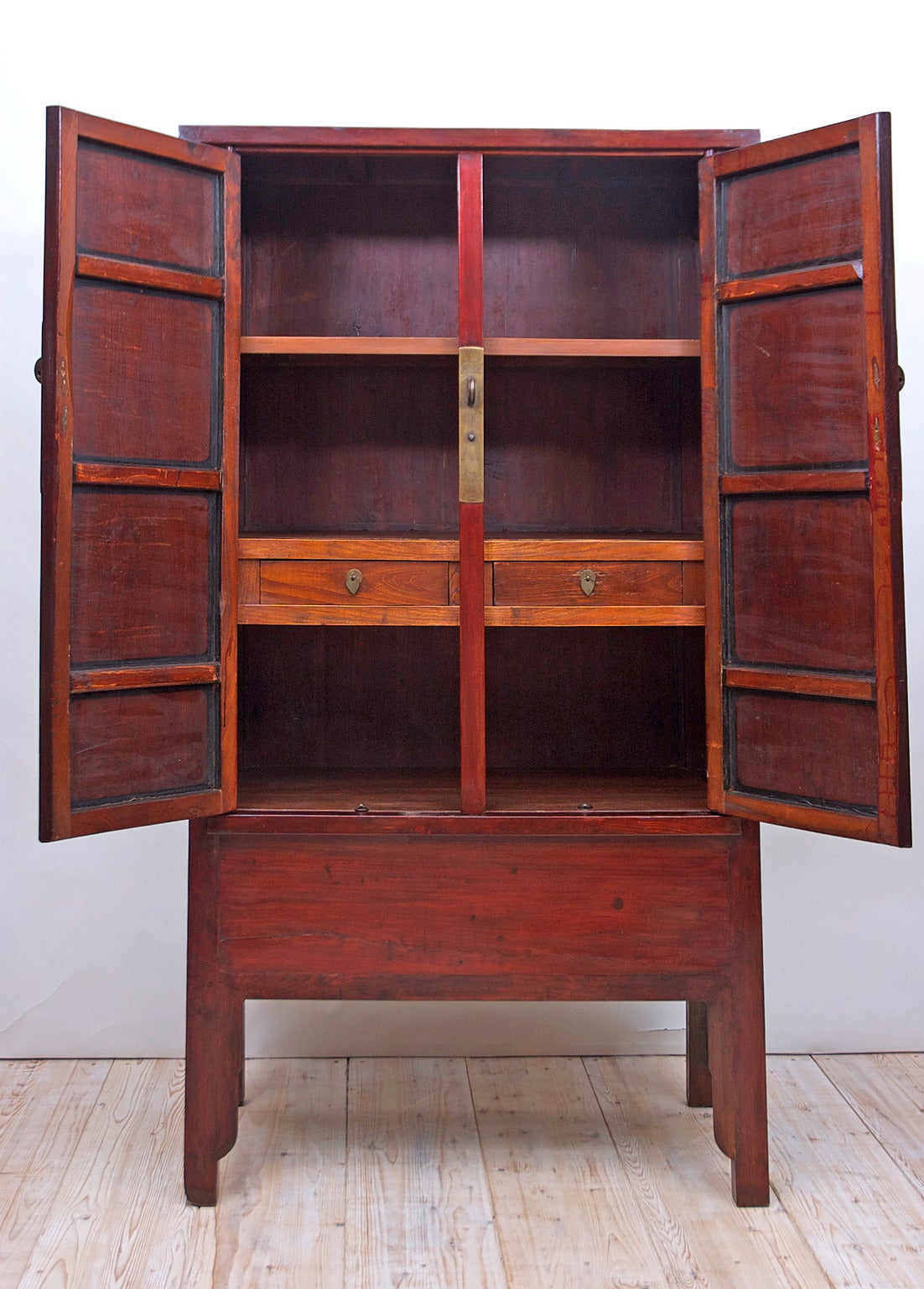 A red-lacquered storage cabinet with two doors. Offers two interior shelves and two drawers with additional storage on the bottom, accessible by lift-top. Original etched brass circular plate and pulls decorated with flowers and birds, Northern