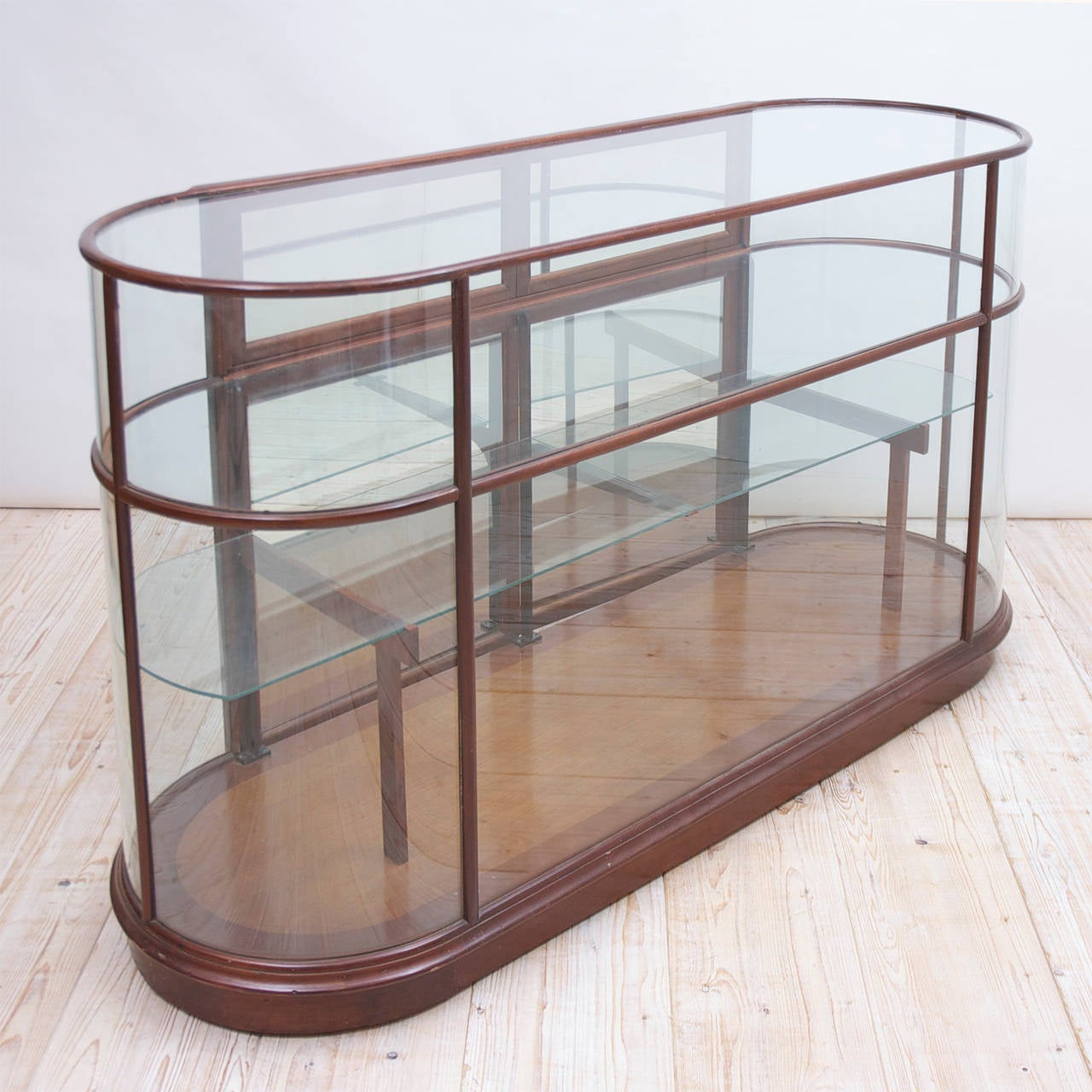 A store display counter with racetrack form. Mahogany framework with shaped glass and glass shelves. Interior mirrors on back doors to create the illusion of being all glass, American, circa 1950. A lovely piece to display lingerie, lace, clothing